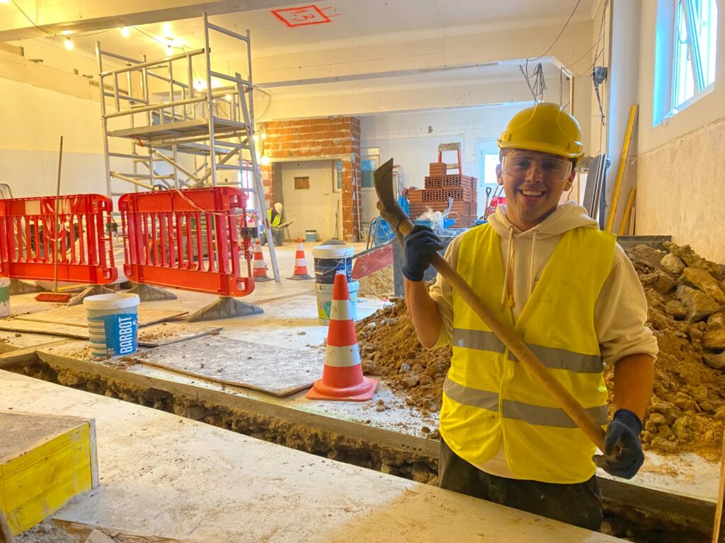 rodrigo sorridente em obra com picareta após abrir calha técnica para cabelagem e tubagens